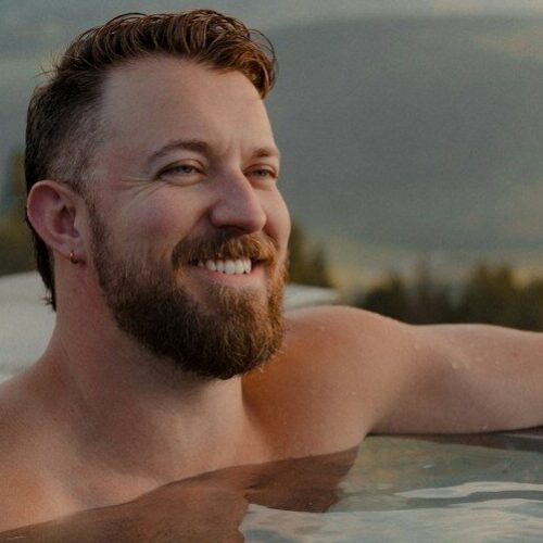 A man with a beard in an infinity pool overlooking mountains in Sorafurcia, Italy